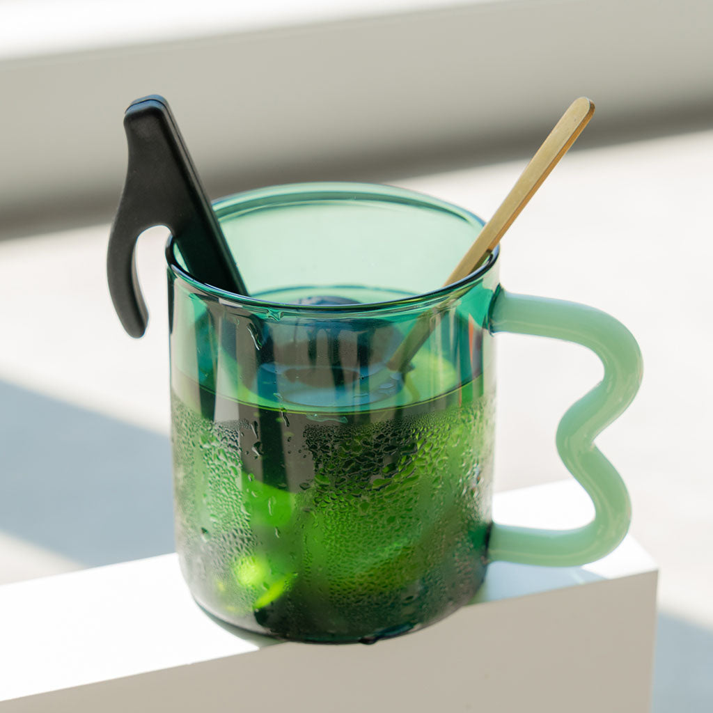 musical note black silicone tea infuser  in a  green glass mug with a stirrer on a white background