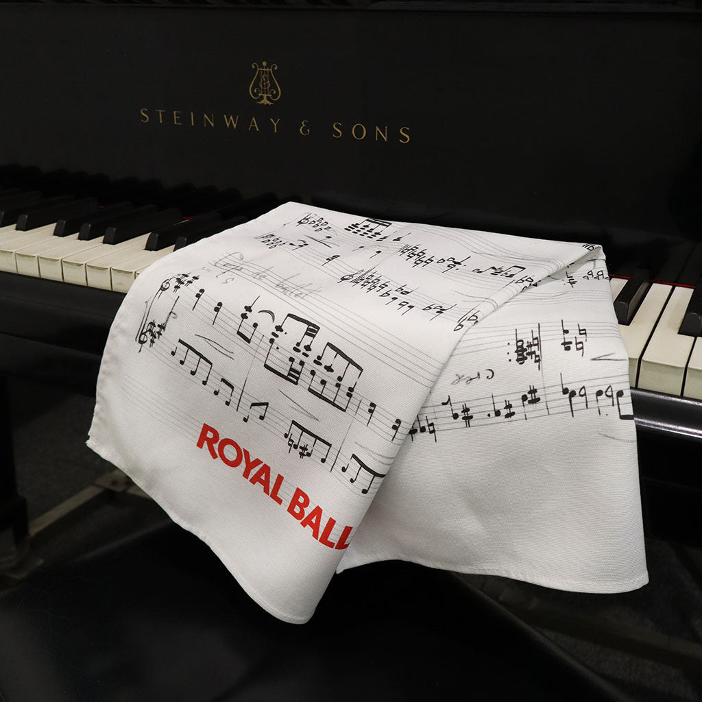 A white fabric tea towel with sheet music notation and the red text 'ROYAL BALLET AND OPERA', draped over the open keys of a black Steinway &amp; Sons piano.