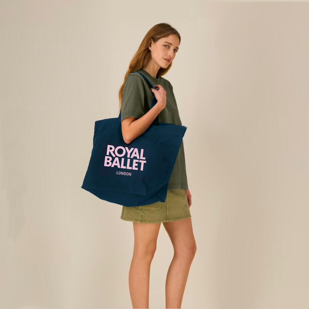 Model wearing navy Royal Ballet London shopper in a green outfit in front of beige backdrop