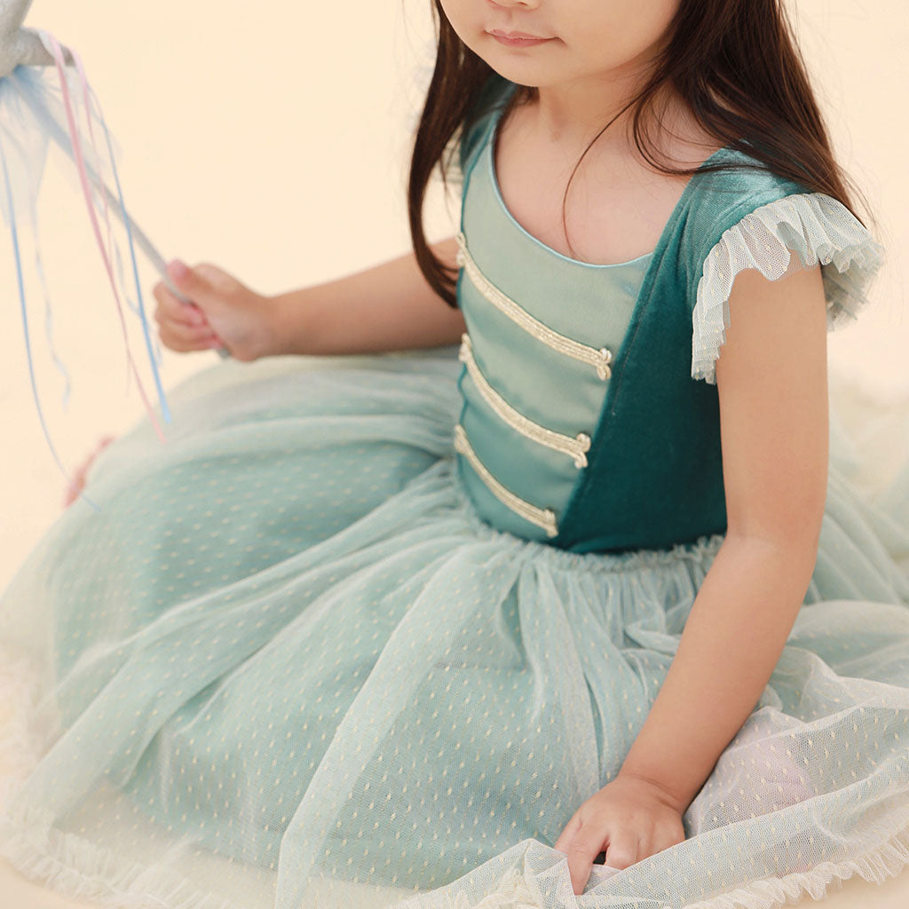Girl in a green Nutcracker ballet dress with a tulle overlay sitting on a beige surface