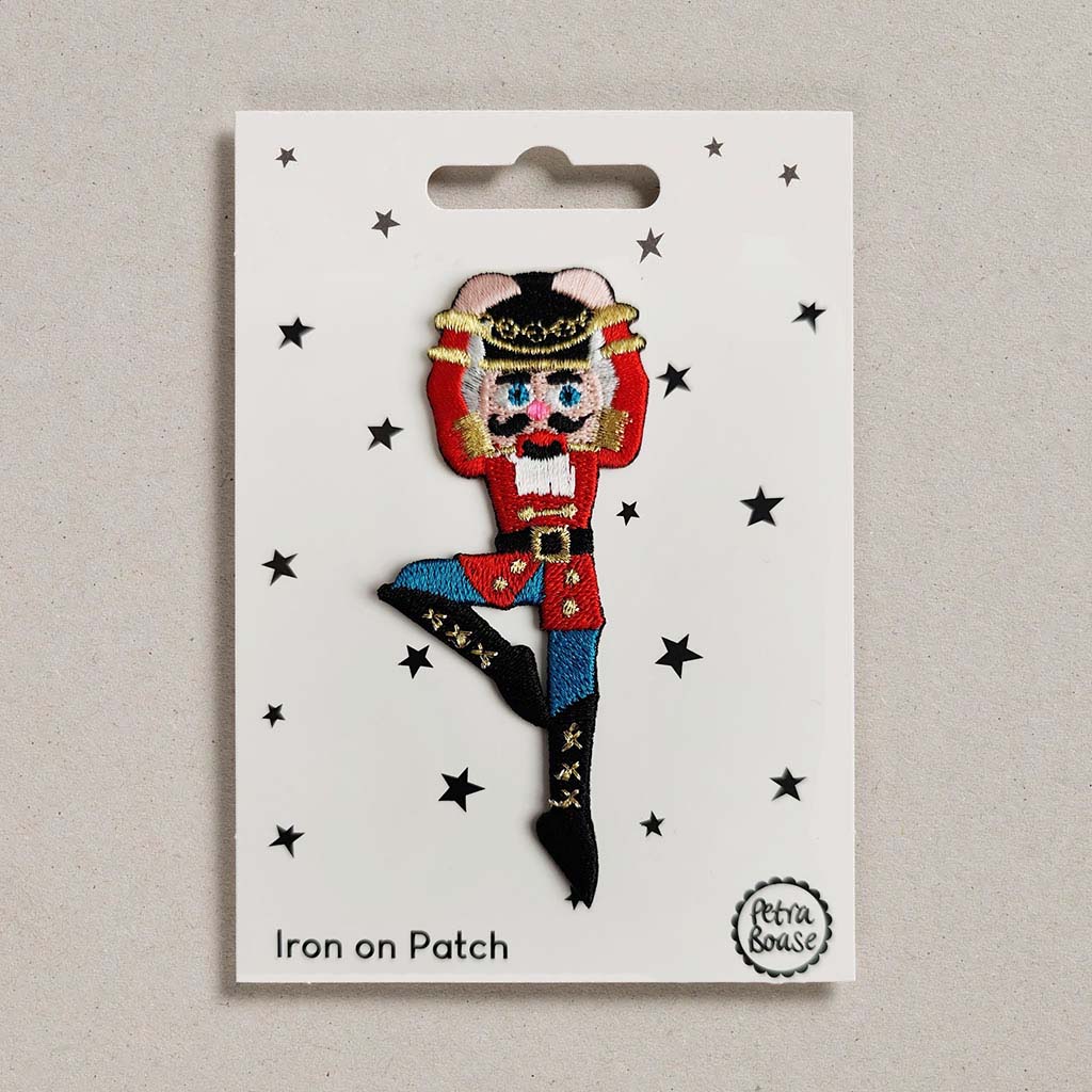 Iron-on patch of a Nutcracker character on a white card with star decorations, brand 'Petra Boase' visible.