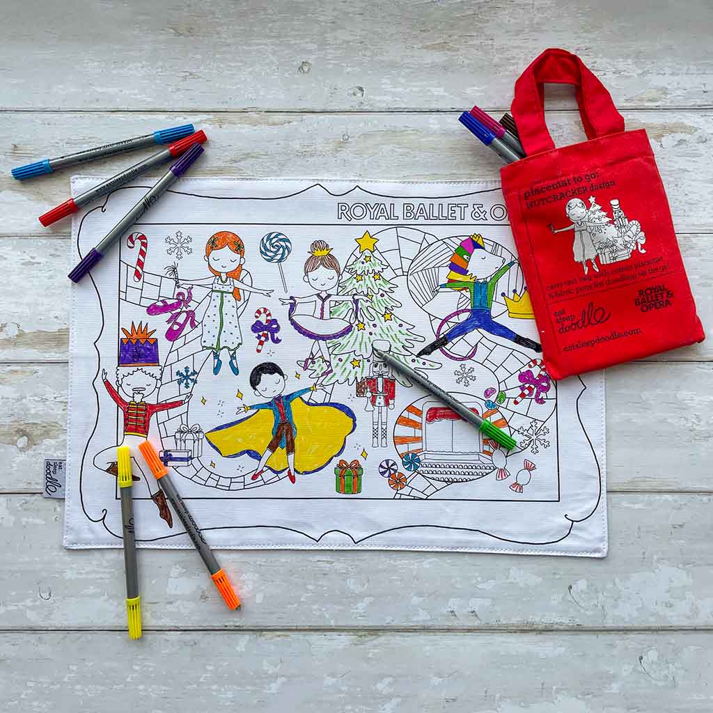 Colouring placemat with The Nutcracker ballet-themed designs, coloured pens, and a red tote bag on a wooden surface.