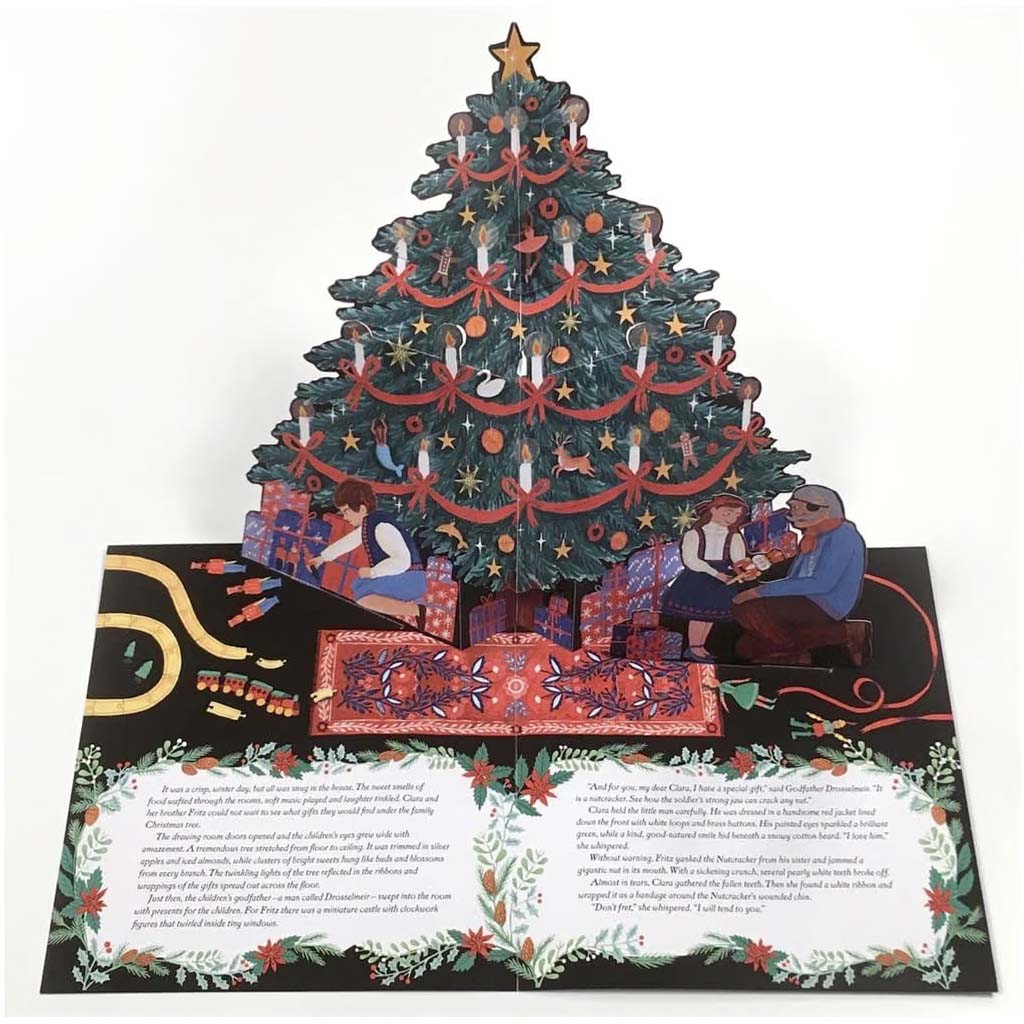 A 3D pop-up book showing a decorated Christmas tree with ornaments, stockings, gifts, and children under a star, with printed text panels on the base against a white background.