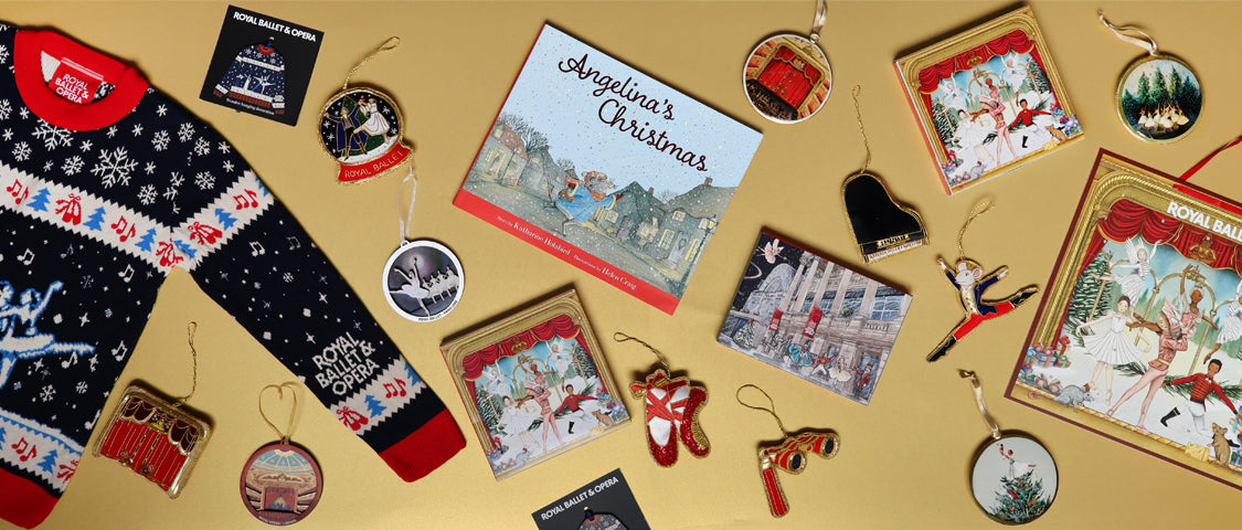 A curated flat lay of christmas-themed merchandise on a warm gold background, including a navy Christmas sweater with red and white patterns, multiple illustrated Christmas decorations, a book titled 'Angeline's Christmas', Christmas card packs, and an advent Calendar.