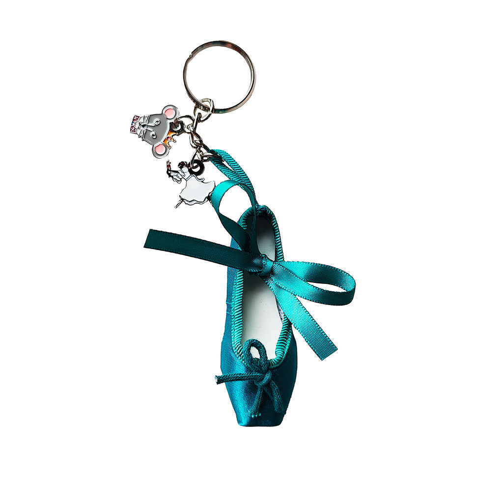 A teal satin ballet shoe keyring with a silver metal key ring and two small dangling charms, a mouse and clara shown on a plain white background.