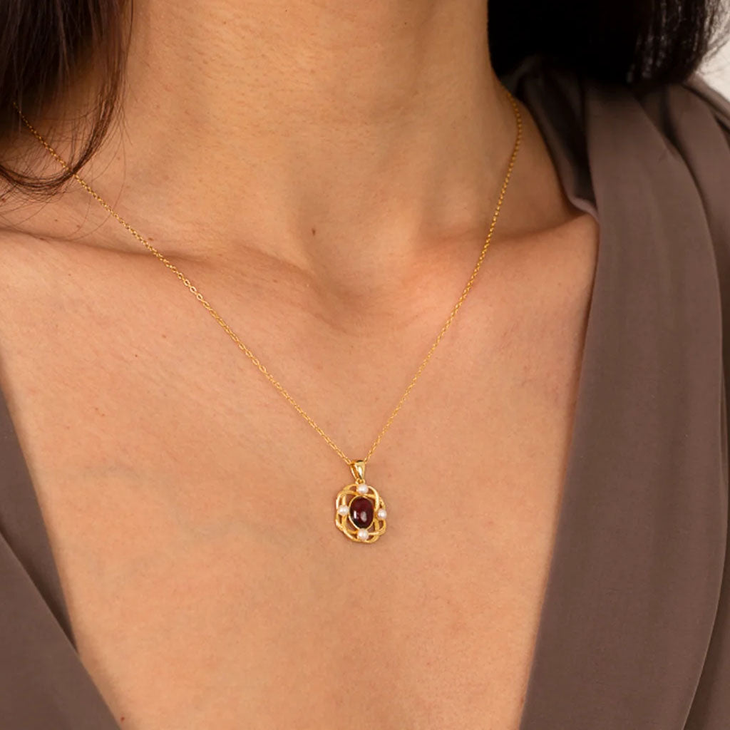 A gold chain necklace with a decorative pendant featuring a central oval red garnet gemstone and small white pearl accents, shown on a plain white background.