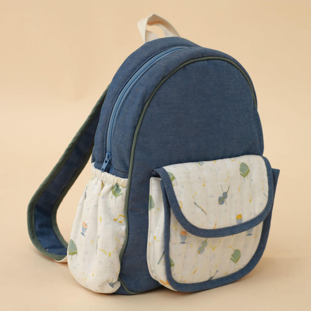 Blue Orchestra backpack with a patterned musical instrument front pocket on a beige background