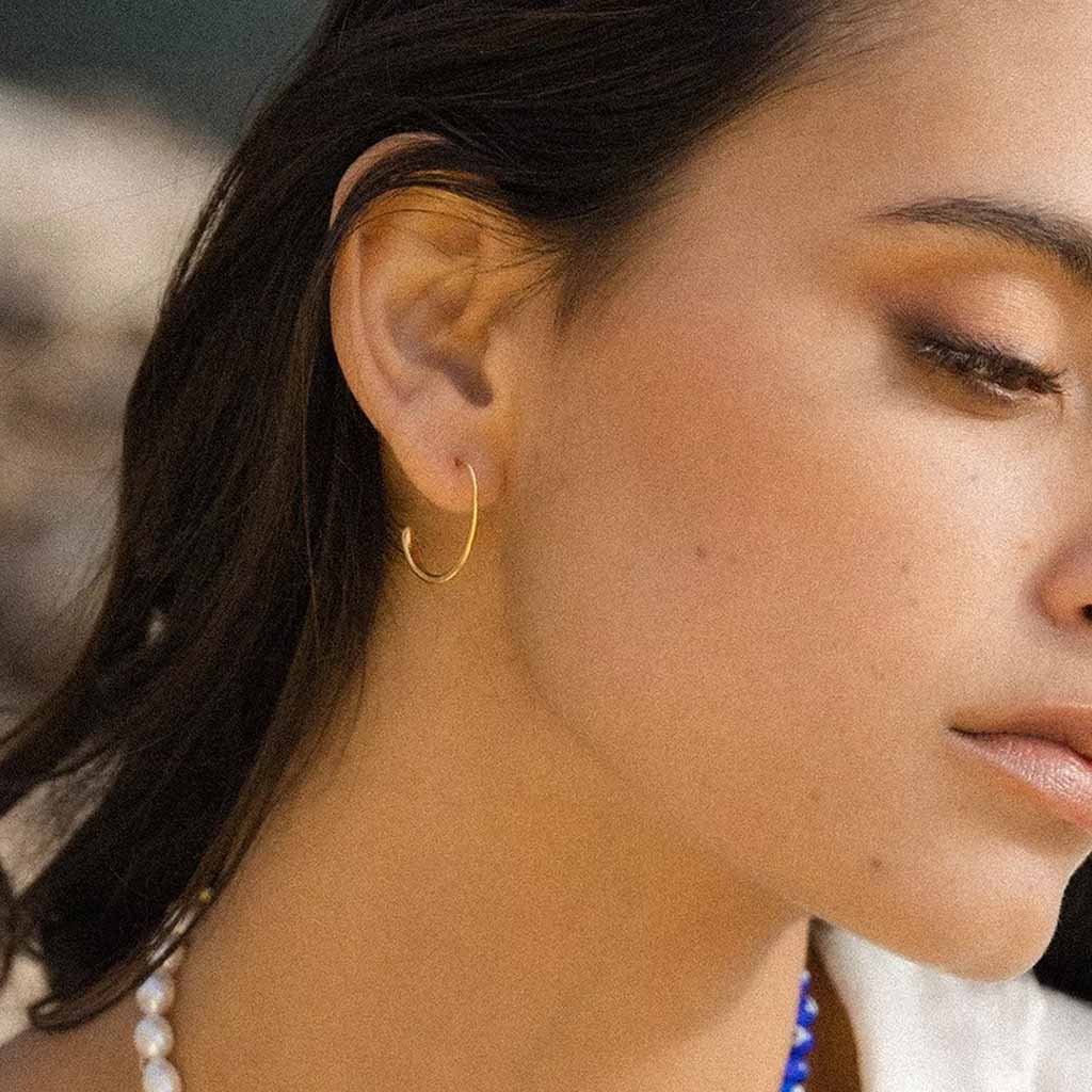 Gold plated brass small oval hoop earrings on a white background