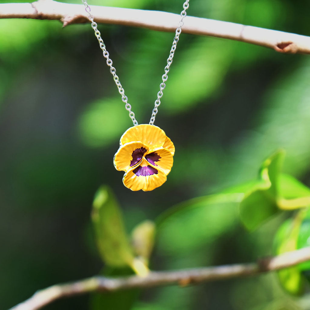 Yellow pansy flower pendant on a chain against a white background