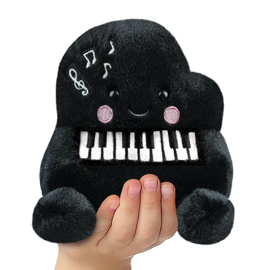 childs hand holding a black piano shaped soft plush top on a white background
