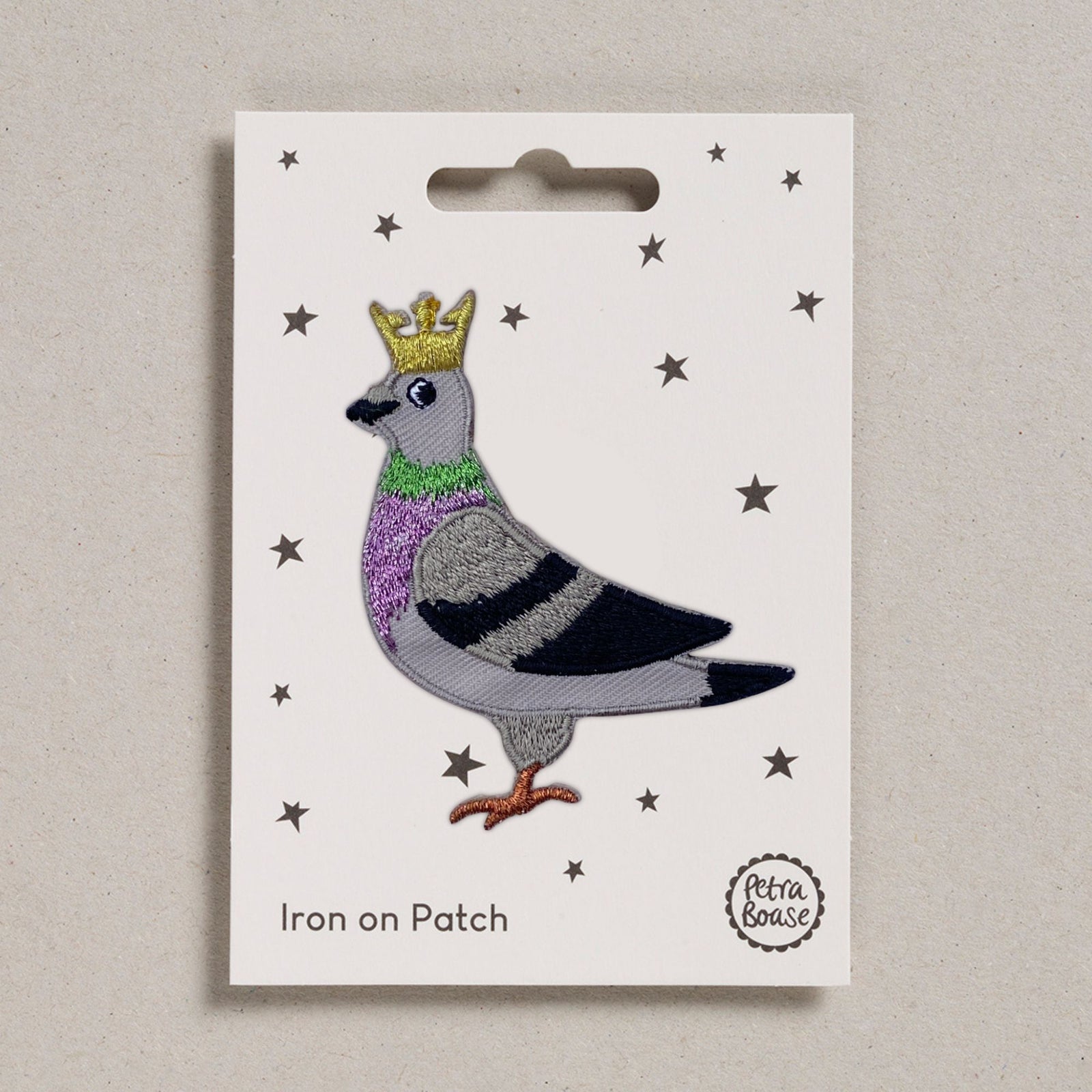 Iron on patch of a pigeon with a crown on a white card with star patterns, brand 'Petra Boase' visible.