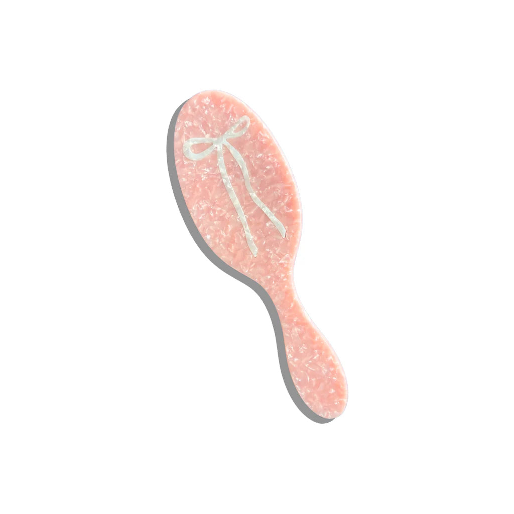 Pink hairbrush with a white bow on a white background