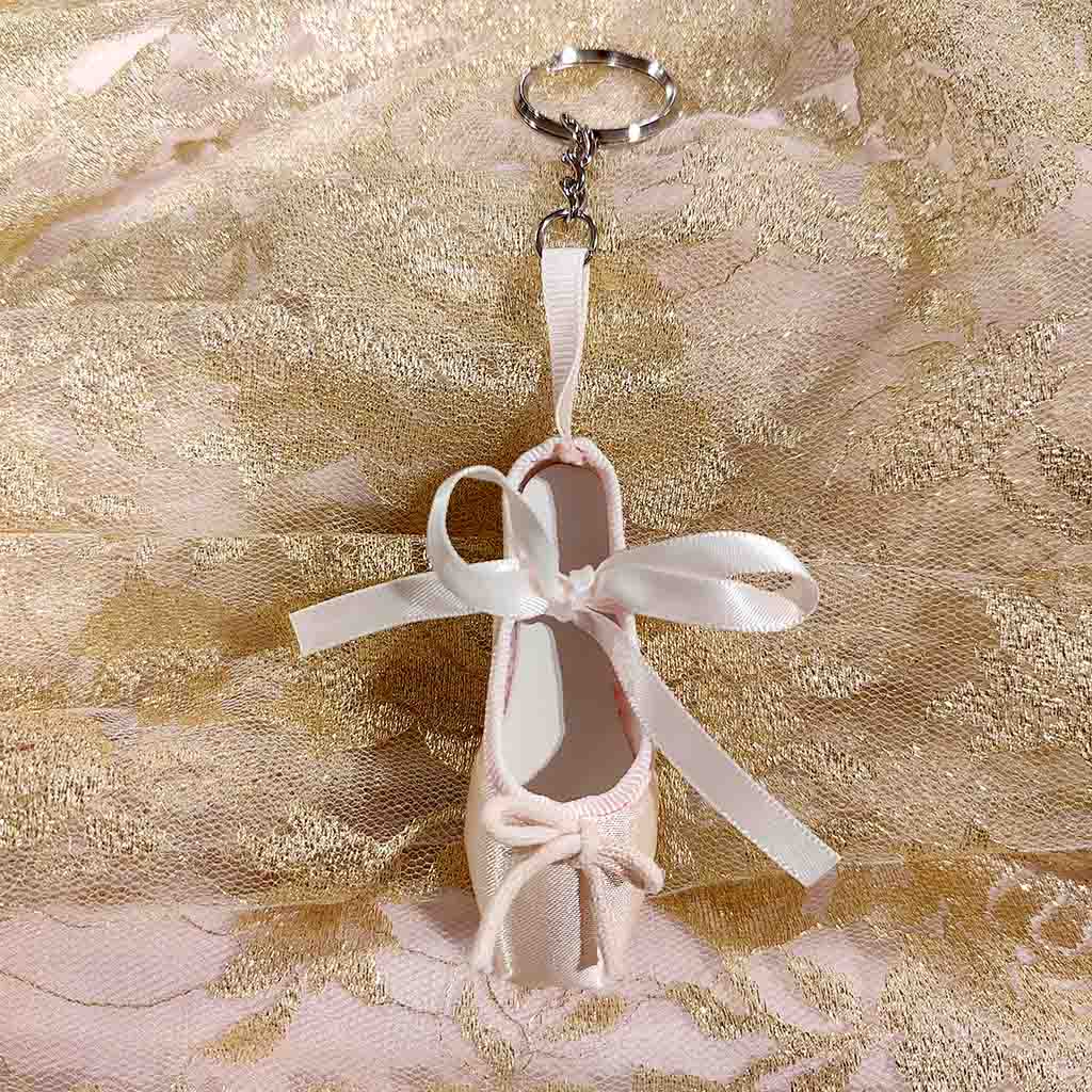 A pink keyring in the shape of a ballet shoe against a white background. The keyring is hanging vertically, suspended by a short metal chain with a larger ring at the top for attaching to keys. There are two pink bows, a larger one about two thirds of the way up the shoe, and a smaller one at the bottom. 