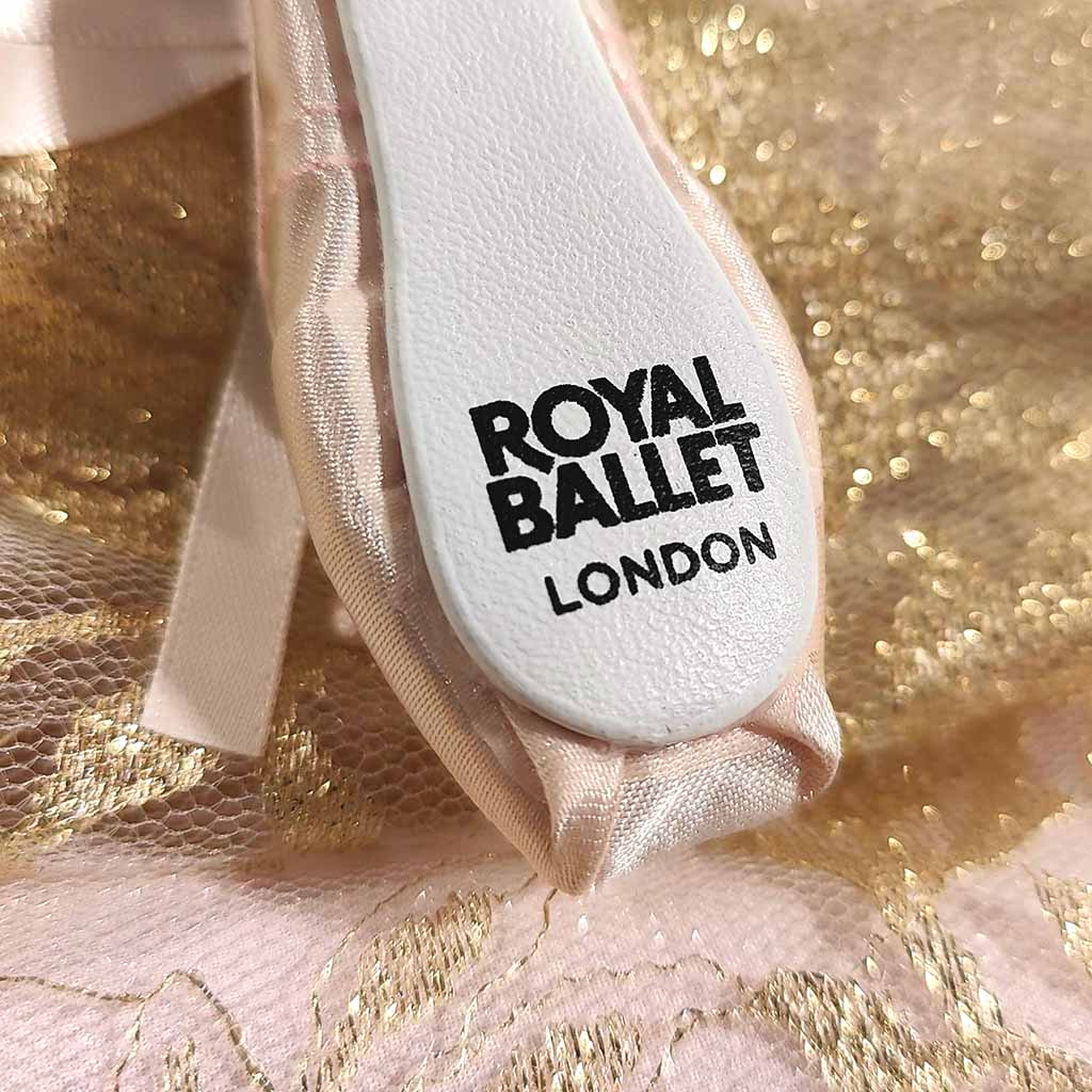 A pink keyring in the shape of a ballet shoe against a white background. The keyring is hanging vertically, suspended by a short metal chain with a larger ring at the top for attaching to keys. There are two pink bows, a larger one about two thirds of the way up the shoe, and a smaller one at the bottom. 