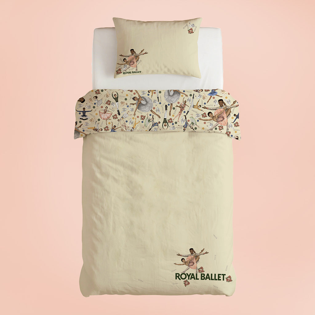 A cream-coloured duvet cover and pillowcase set with a ballet-themed pattern and 'ROYAL BALLET' branding, displayed on a white bed frame against a soft pink background.