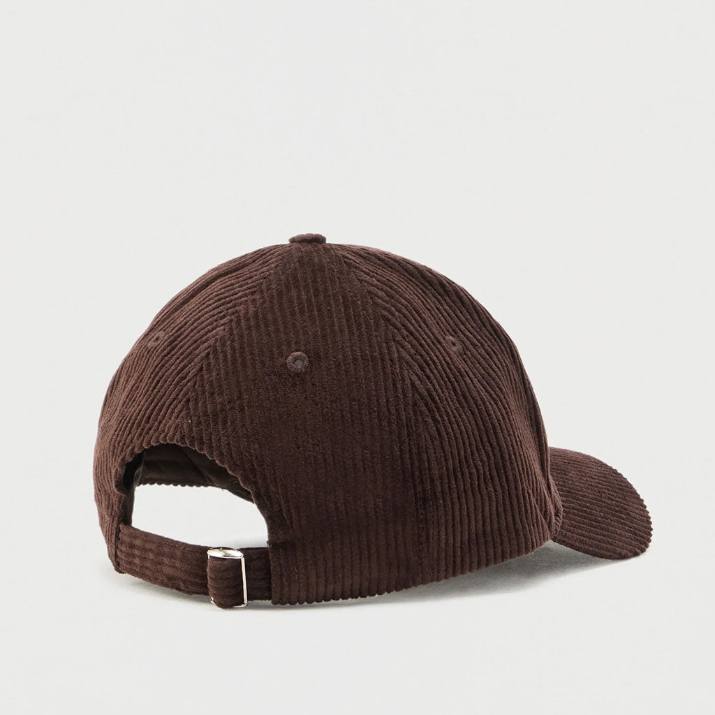 A dark brown corduroy baseball cap shown from a rear three-quarter angle, featuring an adjustable hook-and-loop strap with a silver metal buckle, set against a plain light gray background.