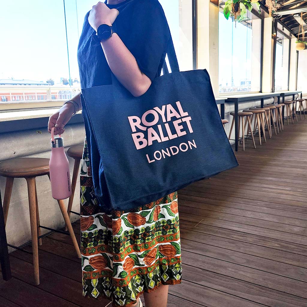 Person holding a denim &#39;Royal Ballet London&#39; tote bag on a terrace