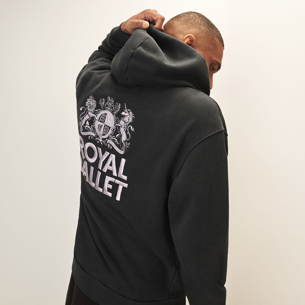 Person wearing a black hoodie with &#39;Royal Ballet&#39; logo on the back against a plain background