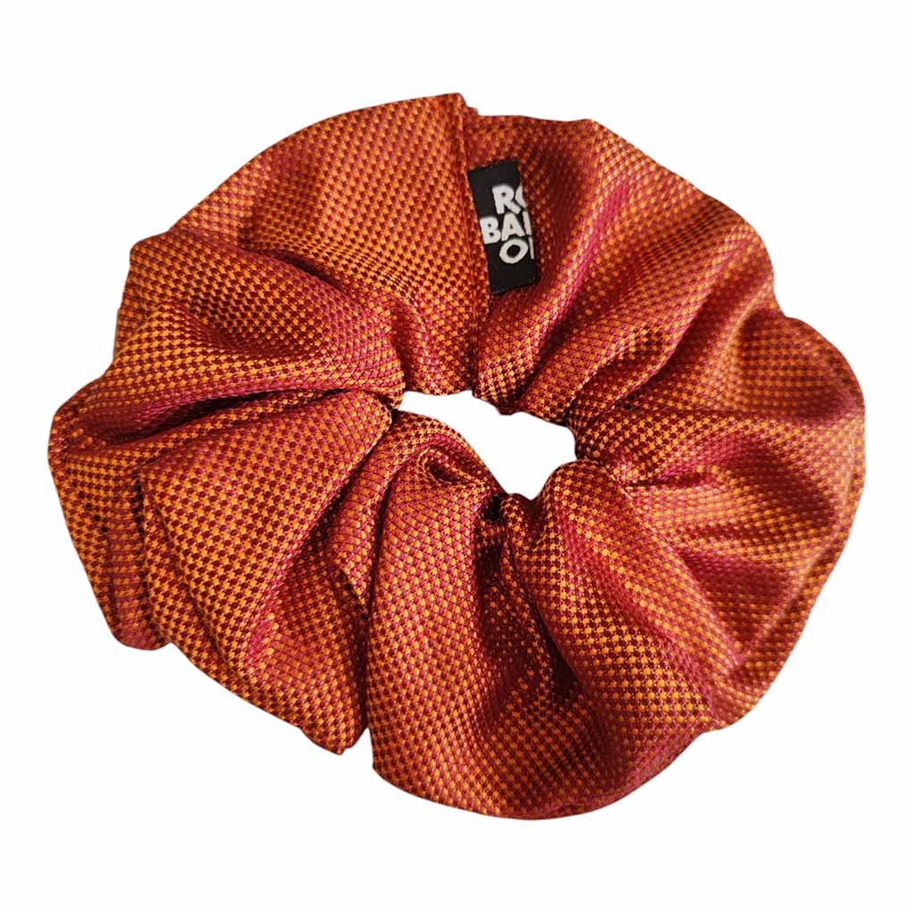 An orange patterned fabric scrunchie with a small black brand tag reading 'RBO' on a plain white background.