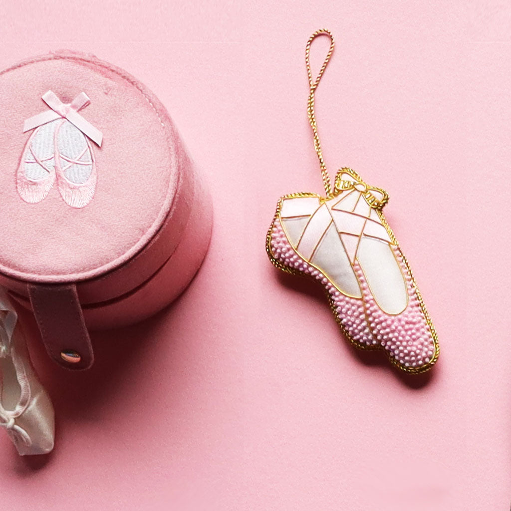 a pink beaded ballet shoe decoration  with gold trim on a white background