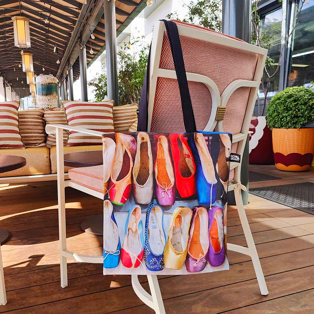 Tote bag with colourful ballet shoes design on the back of a white and pink chair on a terrace