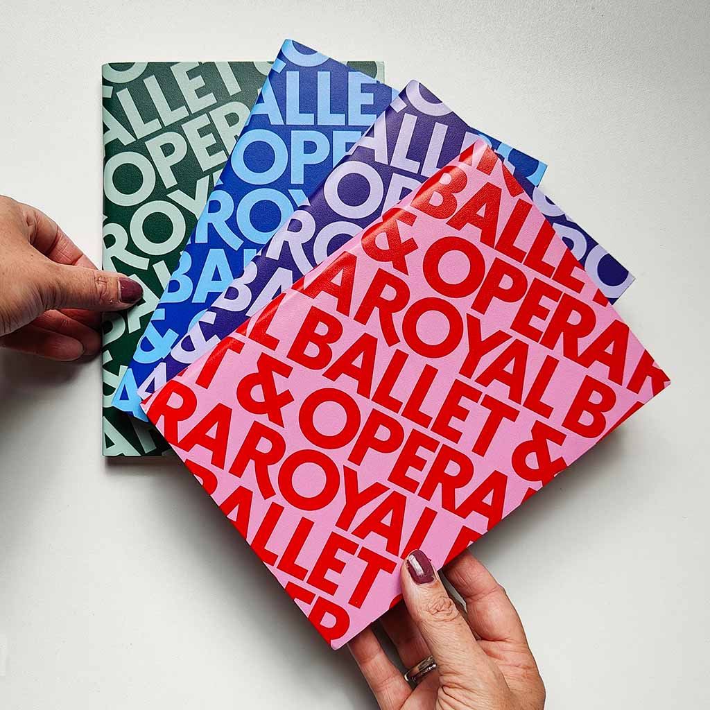 Four colourful notebooks with &#39;Royal Ballet &amp; Opera&#39; text held by hands on a light background
