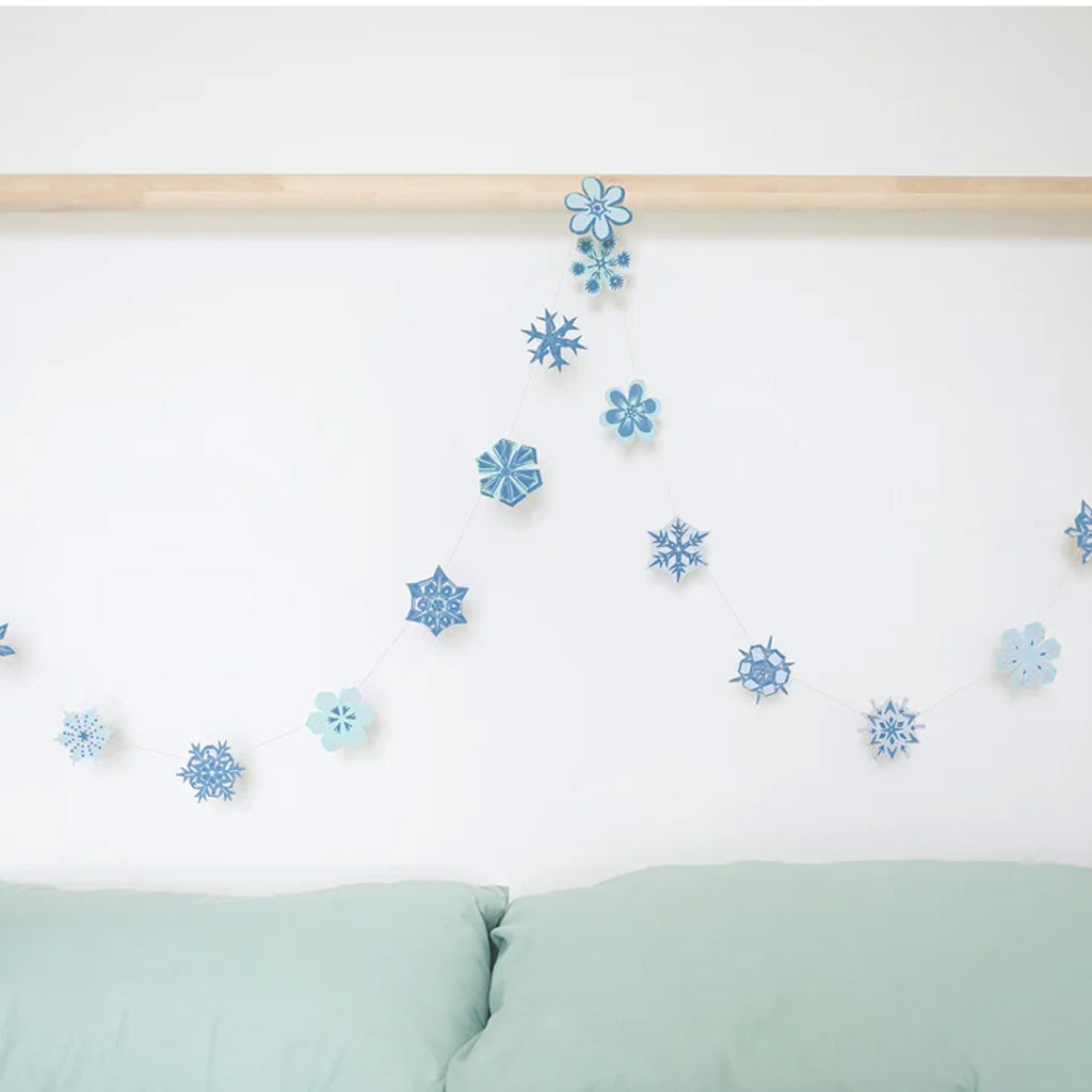 Blue and light blue paper snowflake garland hanging on a white wall above a mint green sofa, with a light wood rail across the top.