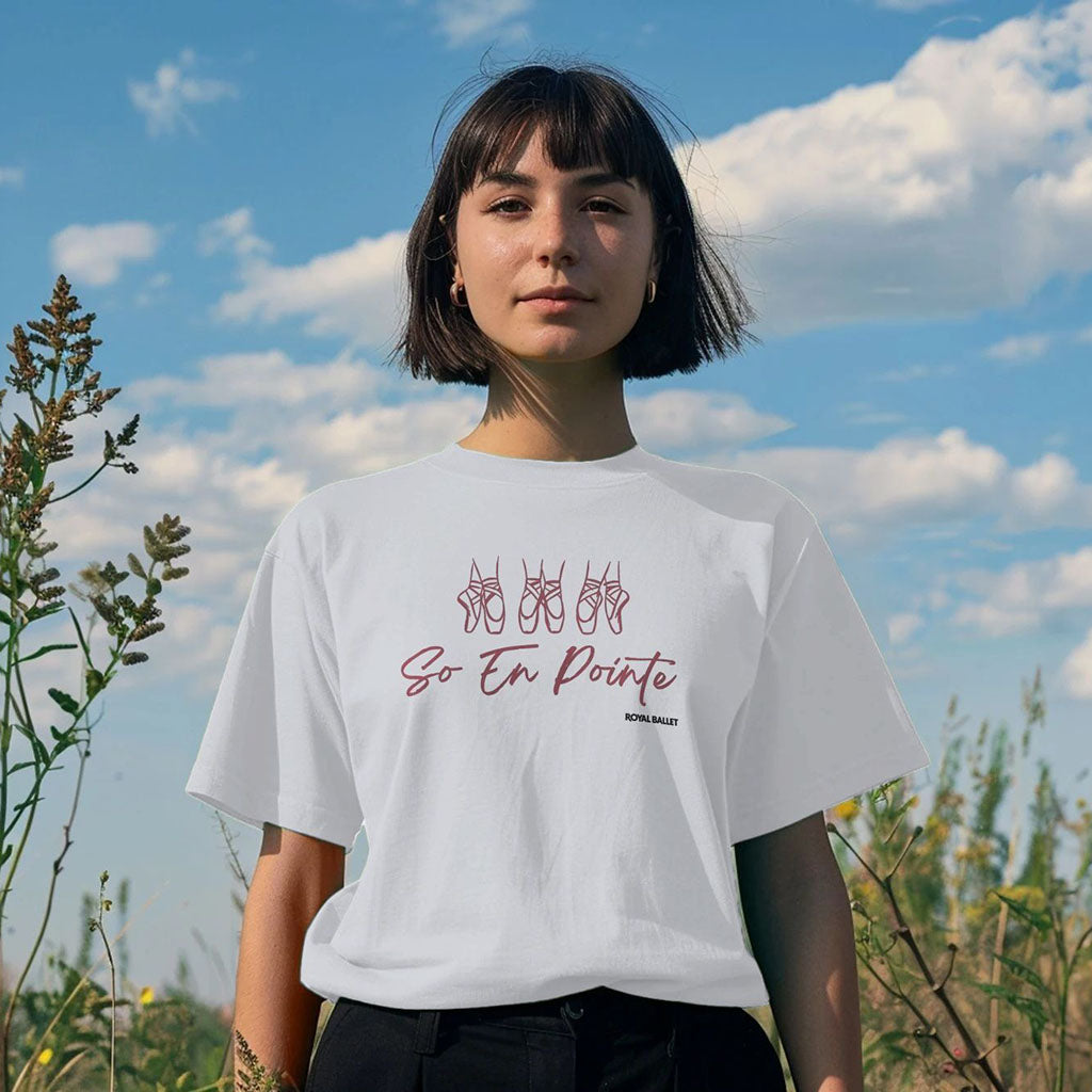 Person wearing a white t-shirt with &#39;So En Pointe Royal Ballet&#39; design outdoors against a blue sky.