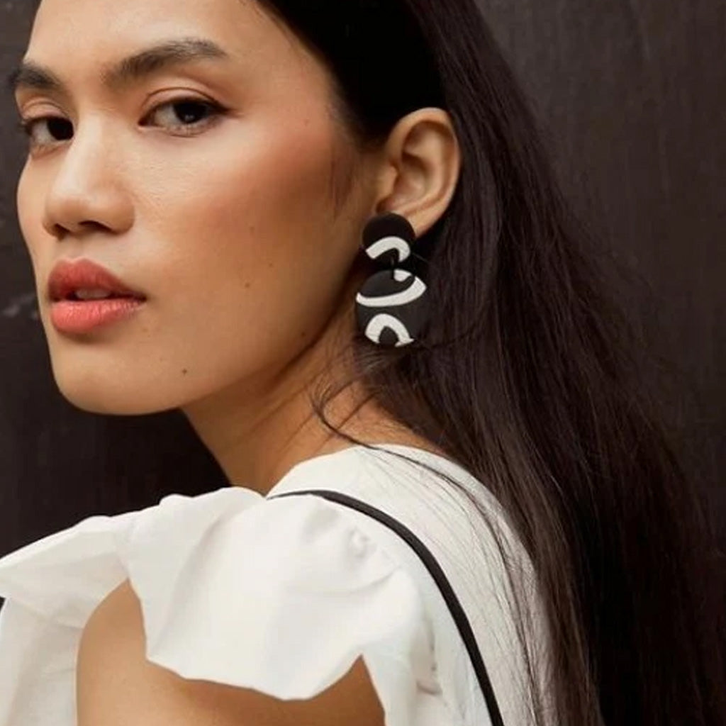 White and  black round abstract earrings featuring two clay discs against a white background