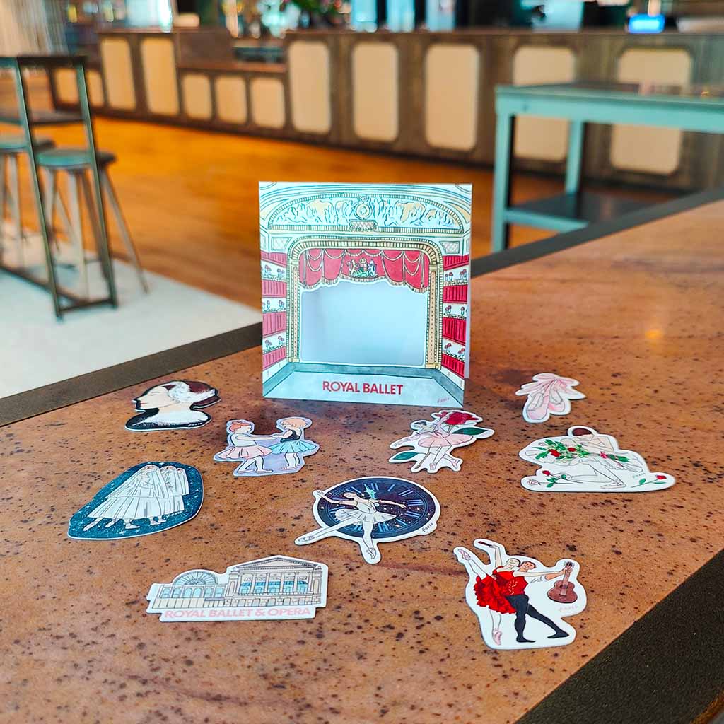 Set of Royal Ballet-themed stickers on a table with a decorative packaging in the background.