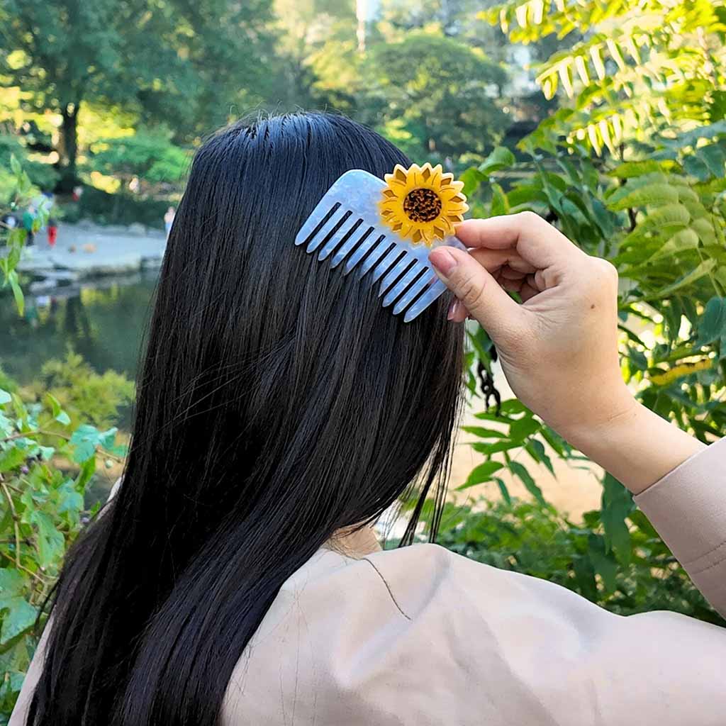 model with long black hair using a sunflower comb in a garden
