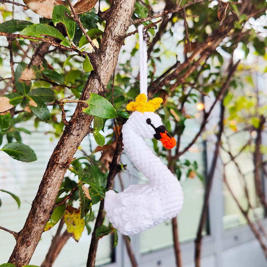 white crochet swan decoration with orange beak and yellow crown on a  tree branch