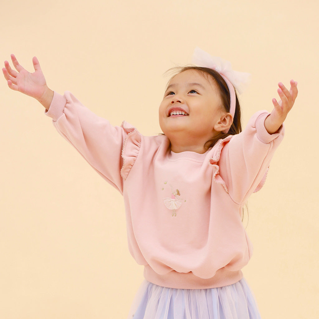 child wearing pink ballerina sweater with embroidered detail and frill sleeves on a beige  background