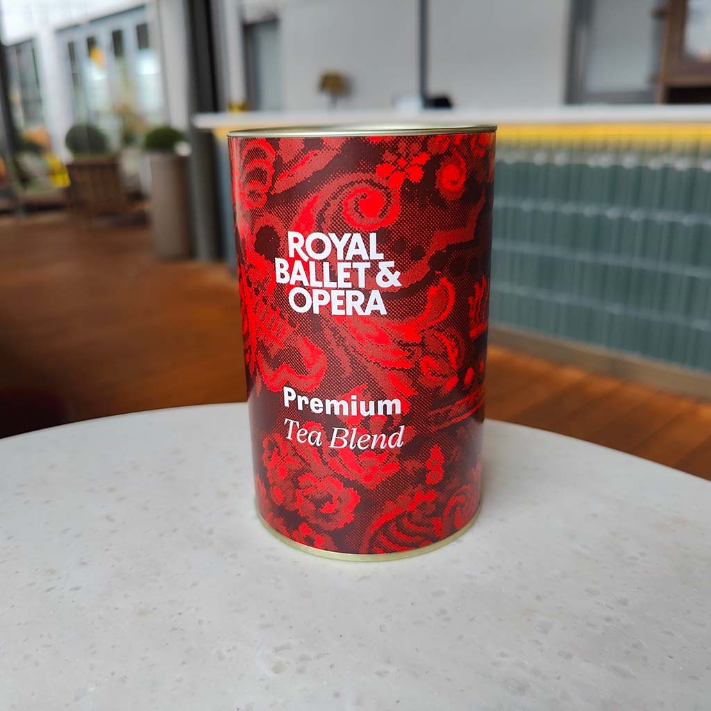 Red can of Royal Ballet &amp; Opera Premium Tea Blend on a white surface with a blurred background.