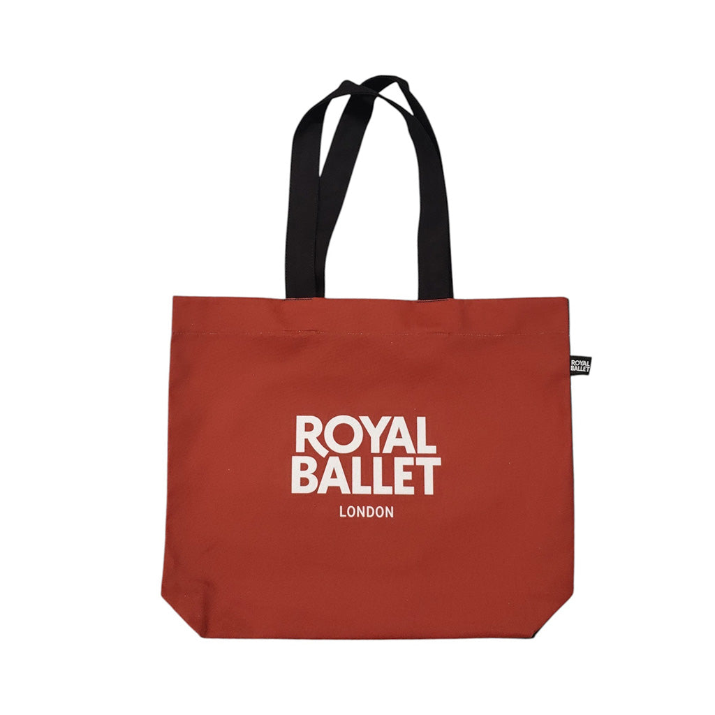 A tote bag featuring a printed graphic of ballerina Marianela Nunez in a red gown on a stage with red curtains, black handles, and a small black side tag with white text.