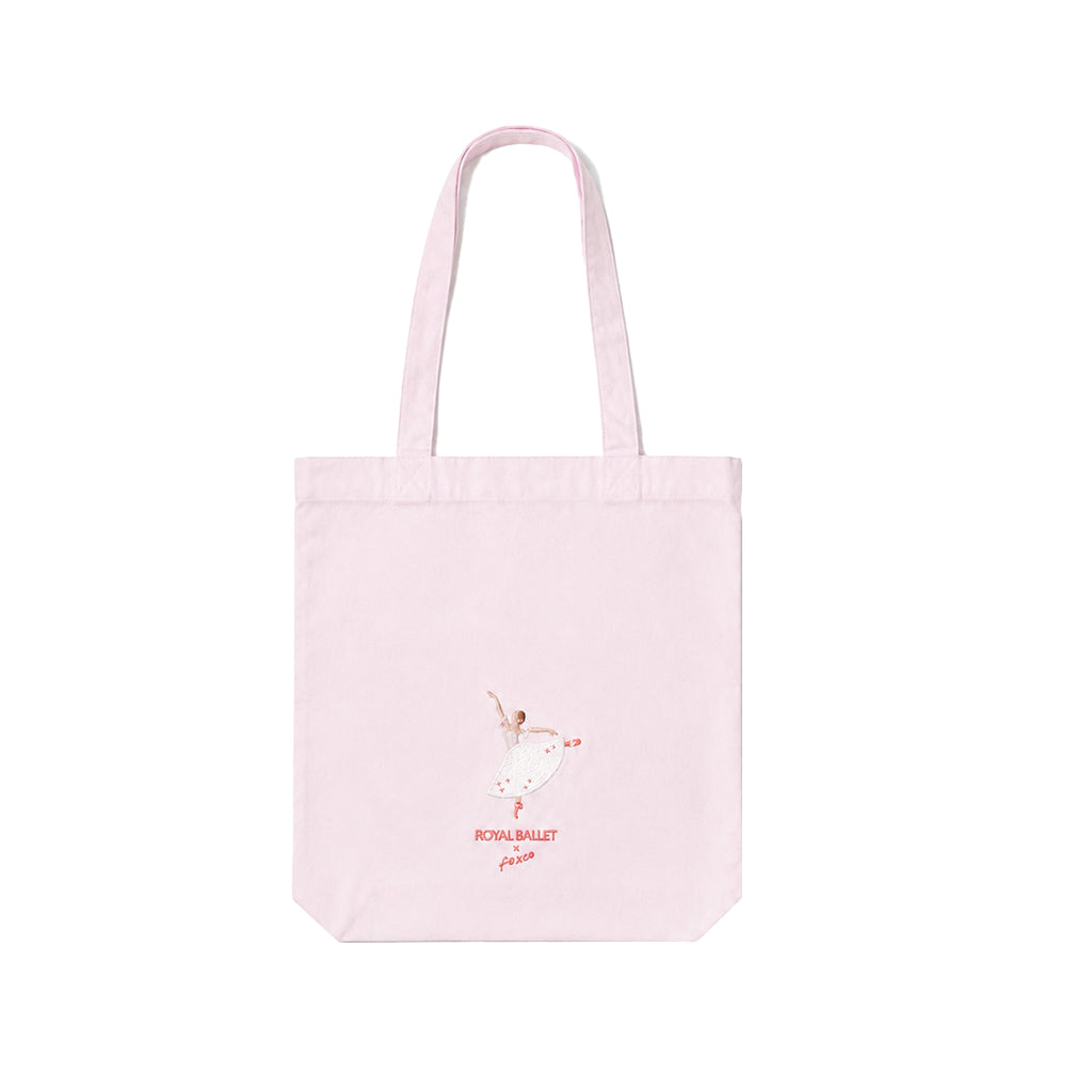 A light pink tote bag with two shoulder straps, featuring a small graphic  embroidered ballerina in a white tutu with dark pink text reading 'ROYAL BALLET x Foxco' below, shown on a plain white background.