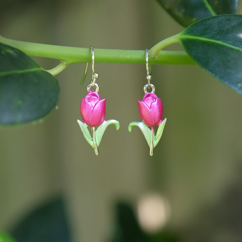 Pink tulip-shaped earrings hanging on a branch with green leaves.