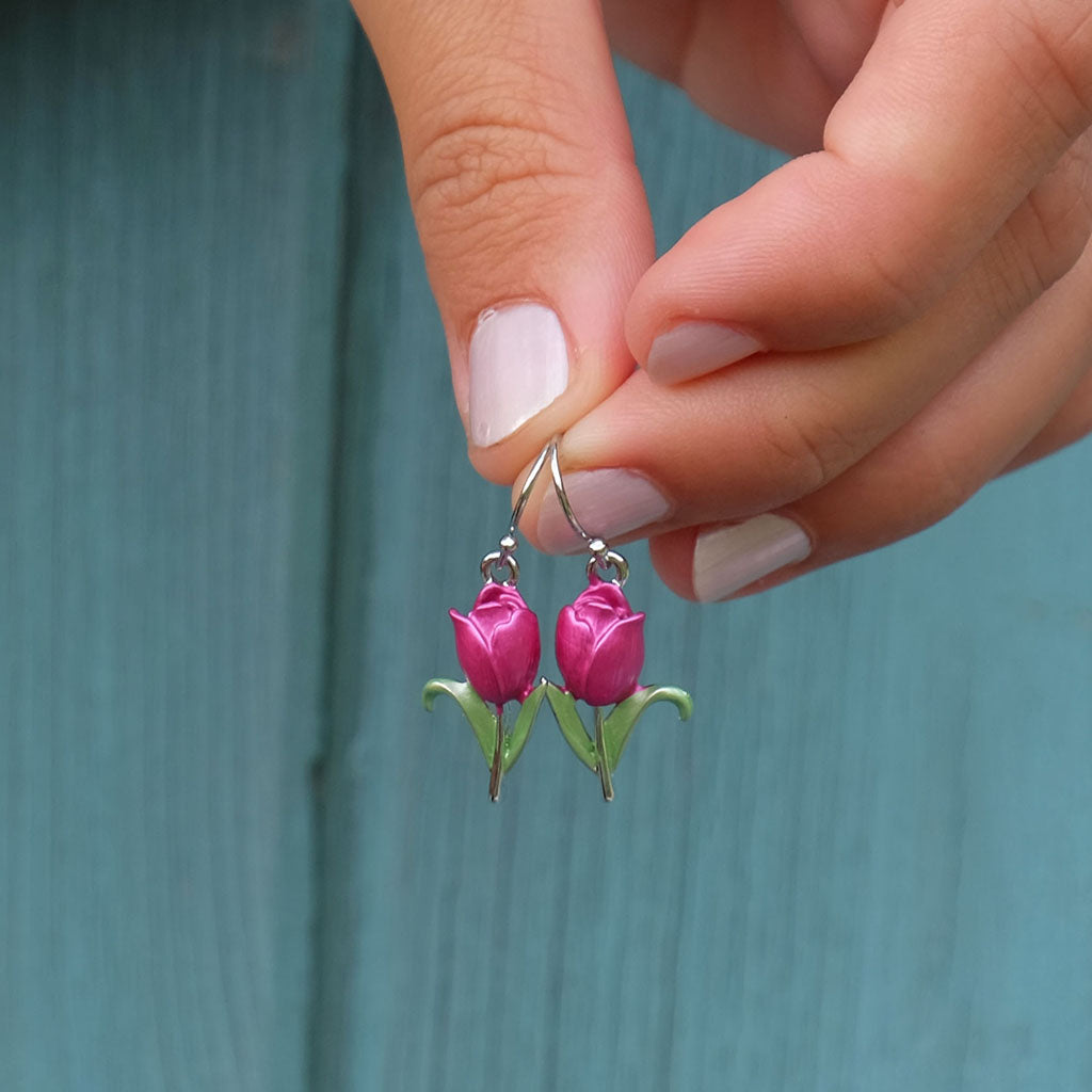 Pink tulip-shaped earrings held between fingers against a teal background