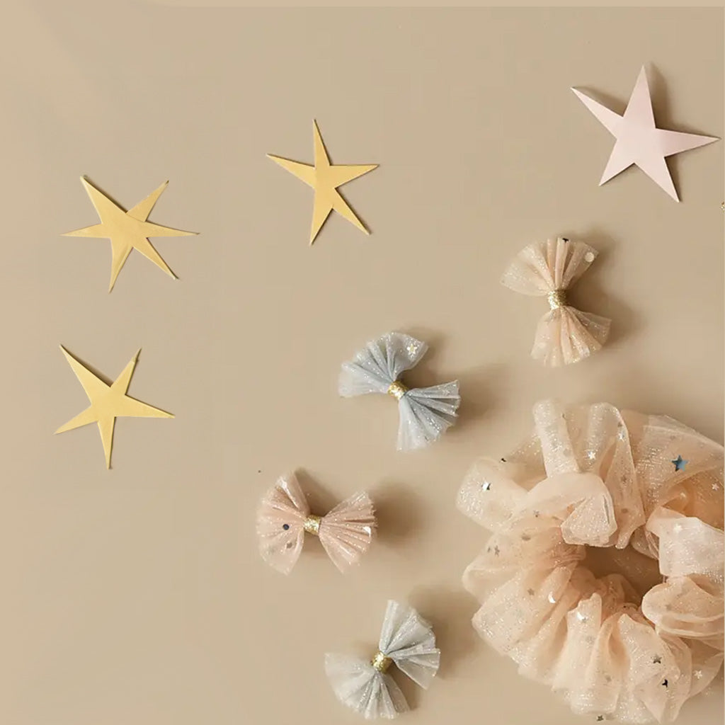 A set of Sparkly Tulle Bow Clips on white card with black dots, against a white background. There are four clips shaped into bows, the top two are a pale pink and the bottom two are a light blue. All four have a glittery gold band around the middle of the bow. 