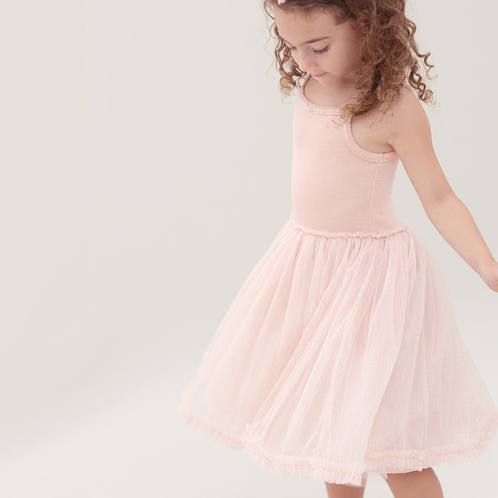 Young girl wearing a pink ballet tutu dress against a plain background