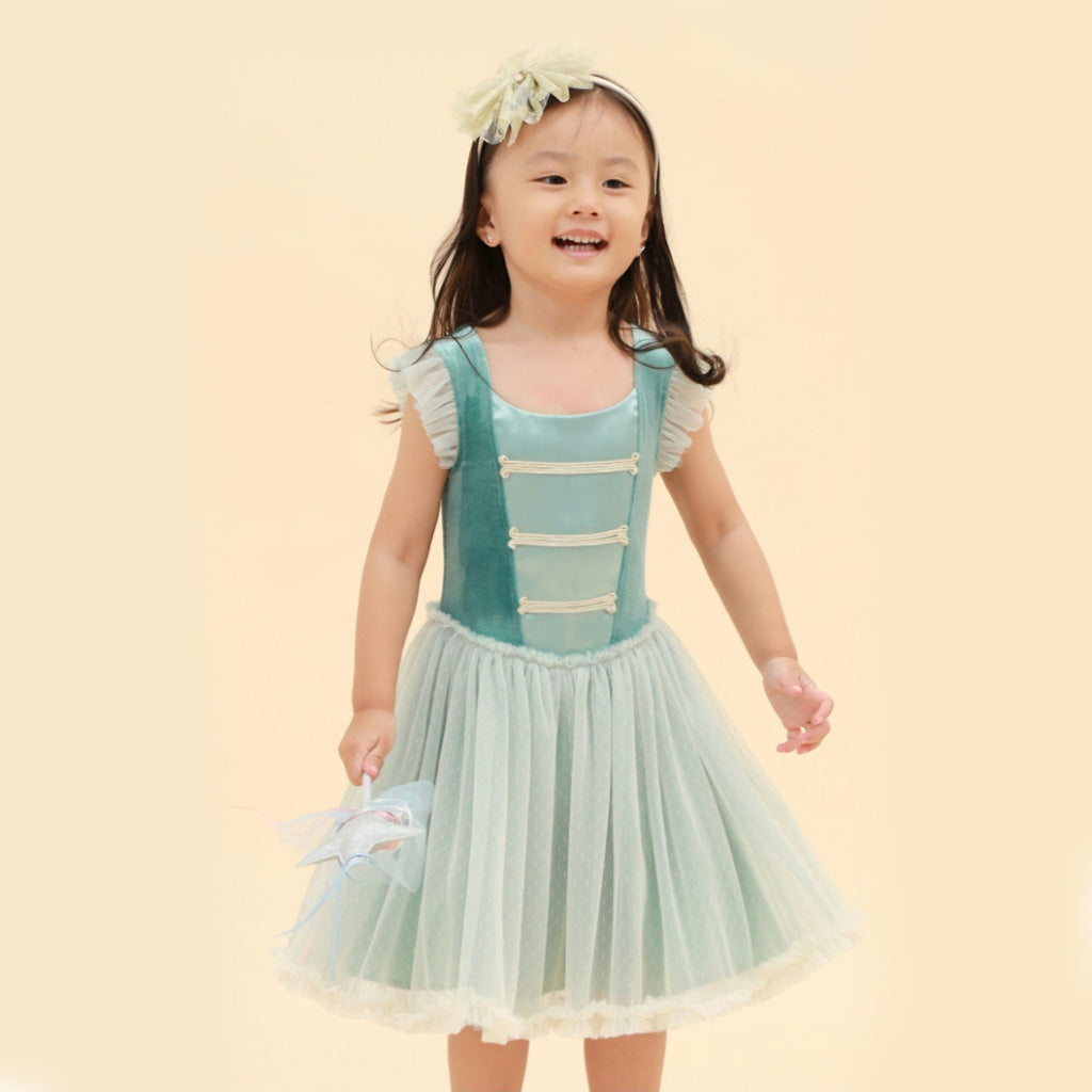 Girl wearing a green Nutcracker dress with ruffled sleeves on a beige background