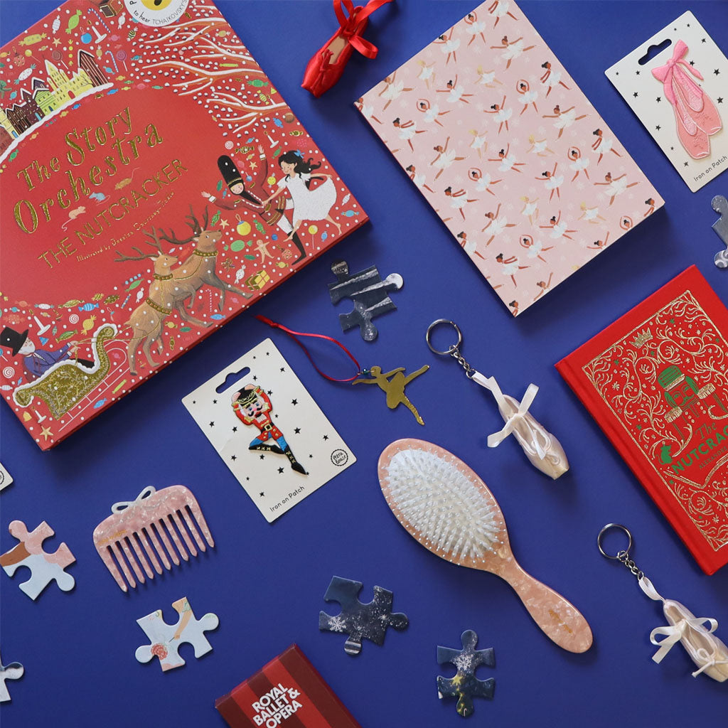 Collection of nutcracker and ballet items including a red books, keyrings, puzzles, and a brush on a blue background.