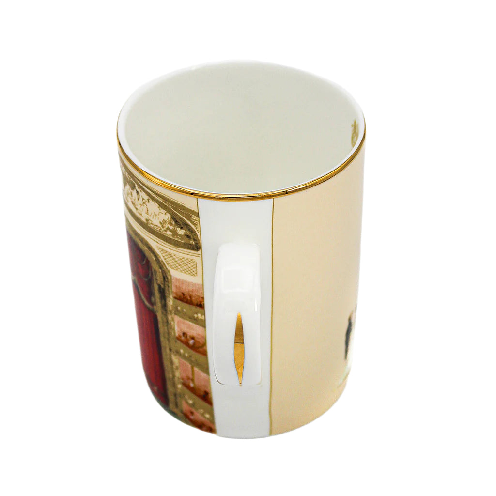 A sideways view of an Auditorium Mug showing the handle side against a white background. The handle is white with a decorative gold line in the middle. On the left side we can see the auditorium design, specifically the edge of the curtains and the auditorium boxes, and on the right we can see the cream colour of the back. 